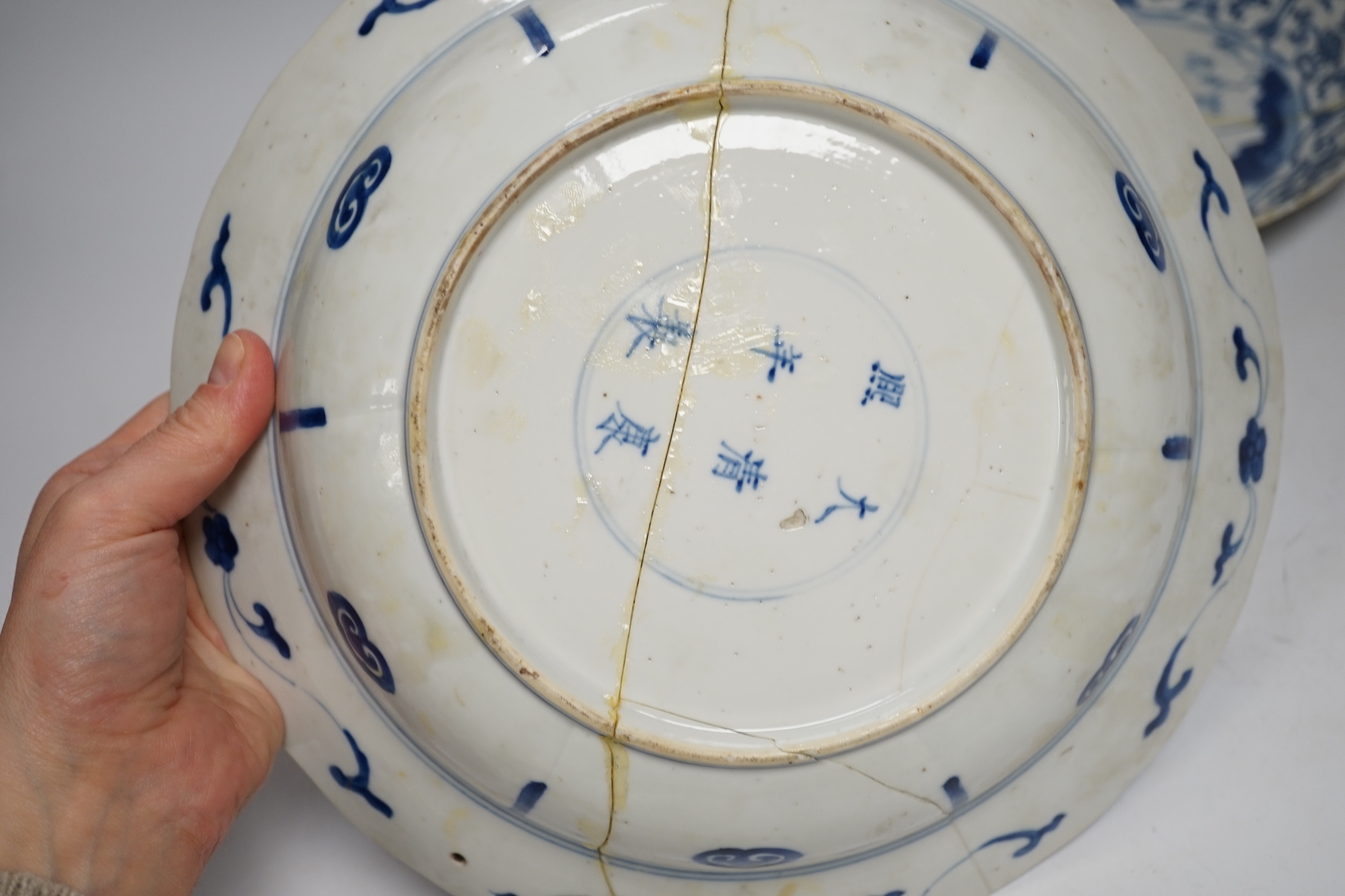 A Chinese blue and white ‘warriors’ bowl, Kangxi mark and period, a similar ‘hunting’ saucer dish, and a famille verte saucer dish, all Kangxi period (3), largest 27cm in diameter